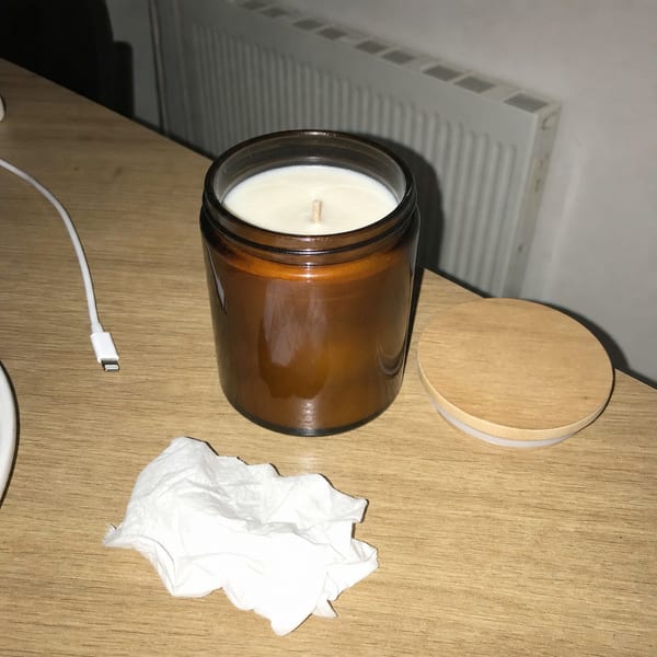 A candle photographed on a table next to a crumpled tissue, lit by a ceiling light